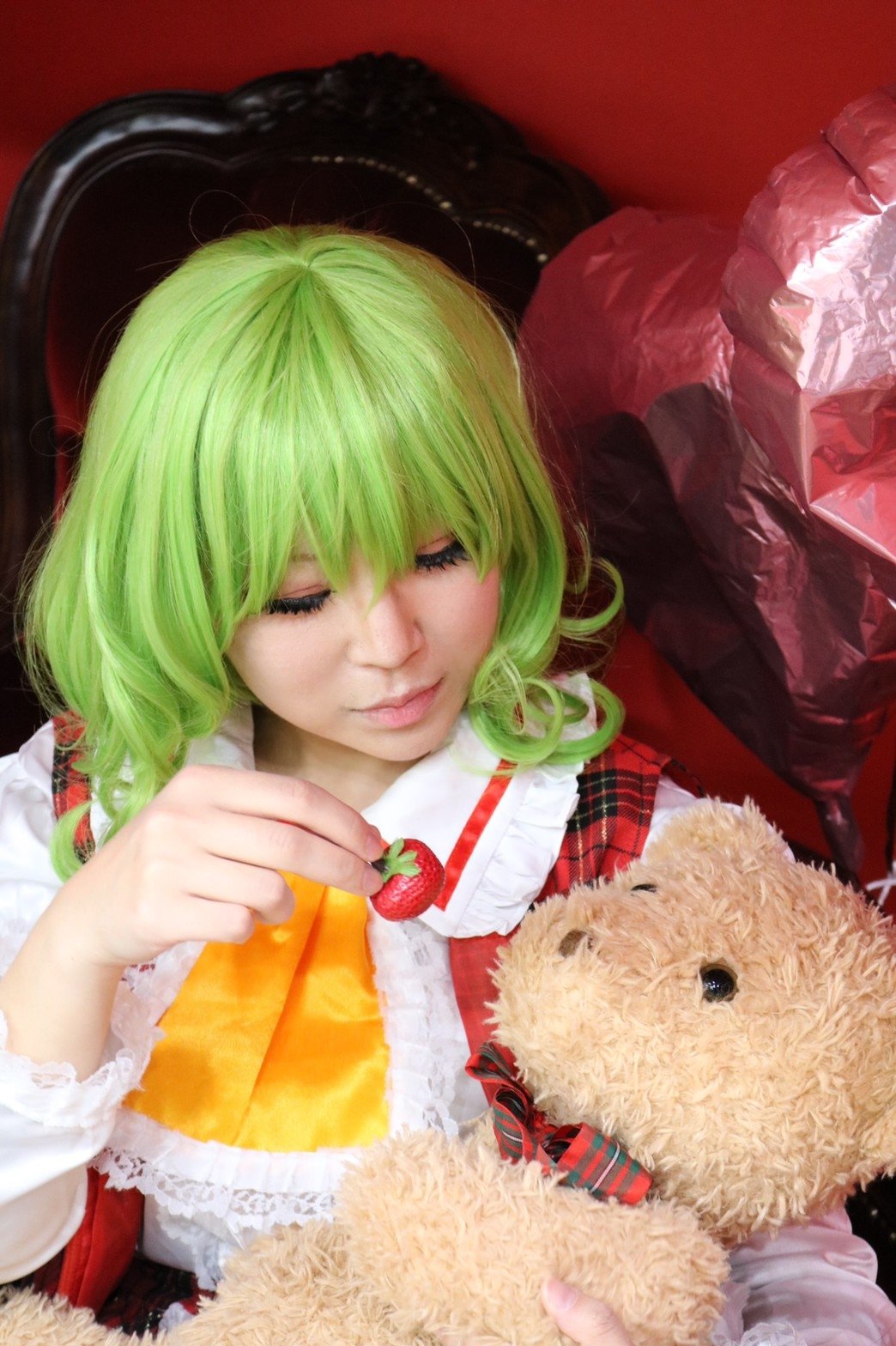 1girl ascot balloon chair closed_eyes commentary_request cosplay cosplay_photo eyelashes feeding food frilled_ascot frilled_shirt_collar frills fruit green_hair hair_between_eyes hand_up heart heart_balloon highres holding holding_food holding_fruit holding_stuffed_toy kazami_yuuka kazami_yuuka_(cosplay) lace_trim photo_(medium) plaid_clothes plaid_vest red_vest short_hair smile solo strawberry stuffed_animal stuffed_toy teddy_bear touhou upper_body vest yellow_ascot