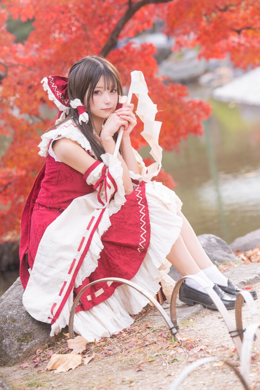 1girl absurdres amanechan08 black_footwear closed_mouth cosplay_photo detached_sleeves frilled_ribbon frills hair_ribbon hair_tubes hakurei_reimu highres long_hair looking_at_viewer outdoors photo_(medium) red_eyes red_ribbon red_shirt ribbon riverbank rock shirt sitting sleeveless sleeveless_shirt smile socks solo touhou tree white_socks