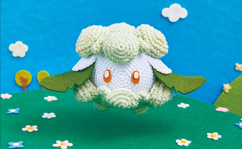 amigurumi_(medium) asako_ito commentary cottonee creature creatures_(company) day english_commentary full_body game_freak gen_5_pokemon nintendo no_humans official_art outdoors photo_(medium) pokemon pokemon_(creature) pokemon_tcg solo third-party_source unconventional_media