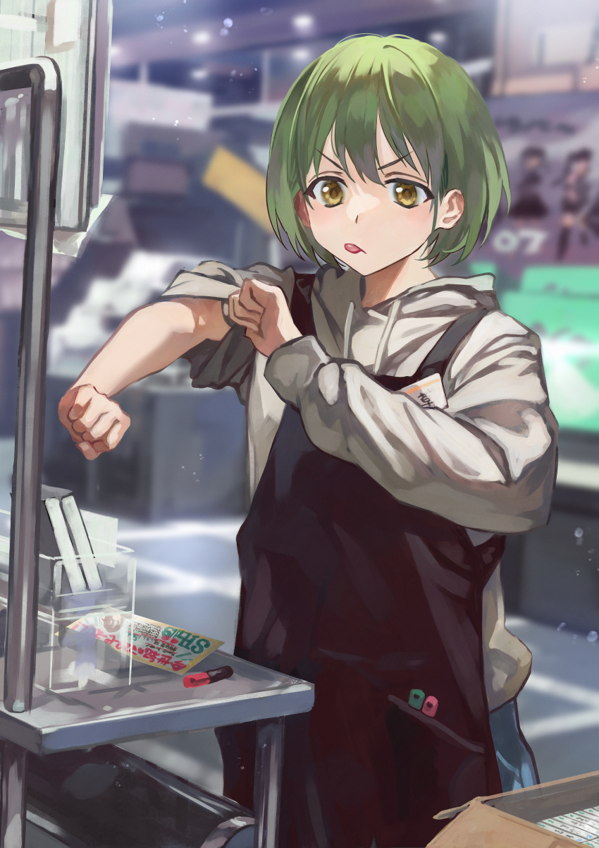 1girl apron black_apron green_hair grey_hoodie highres hood hood_down hoodie idolmaster idolmaster_shiny_colors name_tag nanakusa_nichika otsudou rolling_sleeves_up short_hair solo tongue tongue_out v-shaped_eyebrows yellow_eyes