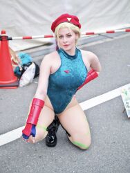 1girl bare_legs bare_shoulders blonde_hair braid breasts cammy_white cammy_white_(cosplay) cosplay curvy earrings fingerless_gloves full_body gloves hands_on_own_knees hat highleg highleg_leotard italian_(nationality) jewelry large_breasts leotard lips long_hair looking_at_viewer photo_(medium) real_life revealing_clothes skindentation sleeveless smile squatting street_fighter thong_leotard twin_braids very_long_hair wide_hips yuriko_tiger