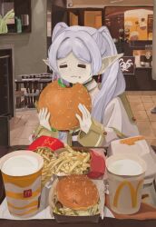  1girl :3 =_= burger capelet cup dangle_earrings disposable_cup earrings eating elf food food_on_face french_fries frieren gold_trim hands_up highres holding holding_burger holding_food indoors jewelry long_sleeves mcdonald&#039;s naaga_sonomono parted_bangs photo_background pointy_ears restaurant sitting sleeve_cuffs solo sousou_no_frieren twintails white_capelet white_hair 