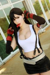 Rule 34 | 1girl, adami langley, armpits, artist name, belt, black hair, breasts, cleavage, color contacts, cosplay, dutch angle, final fantasy, final fantasy vii, large breasts, long hair, looking at viewer, midriff, mouth hold, navel, outdoors, photo (medium), red eyes, skirt, solo, tifa lockhart