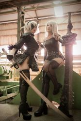 Rule 34 | 2girls, a2 (nier:automata) (cosplay), black dress, black hairband, black legwear, blindfold, boots, breasts, closed mouth, cosplay, dress, elbow gloves, feather-trimmed sleeves, gloves, hair over eyes, hairband, high heel boots, high heels, highleg, juliet sleeves, long hair, long sleeves, looking at viewer, medium breasts, multiple girls, nier, nier:automata, nier (series), photo (medium), puffy sleeves, shiny clothes, short hair, side slit, skindentation, thigh boots, thighhighs, vambraces, white hair, 2b (nier:automata), 2b (nier:automata) (cosplay), a2 (nier:automata)