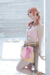 Rule 34 | 1girl, bracelet, building, cosplay, female focus, final fantasy, final fantasy xiii, jewelry, leaning, midriff, necklace, oerba dia vanille, oerba dia vanille (cosplay), photo (medium), pink shirt, shirt, skirt, solo, twintails