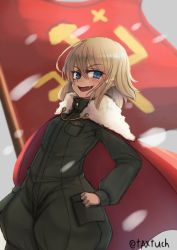 Rule 34 | 10s, 1girl, blonde hair, blue eyes, blurry, blurry background, blush, cape, commentary, emblem, fang, flag, girls und panzer, green jumpsuit, hand on own hip, highres, jumpsuit, katyusha (girls und panzer), light blush, long sleeves, looking at viewer, military, military uniform, one-hour drawing challenge, open mouth, pravda (emblem), pravda military uniform, red cape, red flag, short hair, short jumpsuit, smirk, solo, standing, tacch, twitter username, uniform
