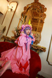 Rule 34 | 1girl, asian, bow, chandelier, cosplay, couch, crescent, dress, female focus, hat, highres, kneeling, long hair, looking back, mirror, mob cap, patchouli knowledge, photo (medium), purple hair, red upholstery, ribbon, robe, slippers, solo, table, tenshi myu, thighhighs, touhou