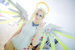 Rule 34 | 1girl, blonde hair, blue eyes, clothing cutout, cosplay, dutch angle, halo, highres, indoors, lana rain, leotard, mechanical wings, mercy (overwatch), mercy (overwatch) (cosplay), overwatch, overwatch 1, photo (medium), side cutout, smile, solo, white leotard, wings