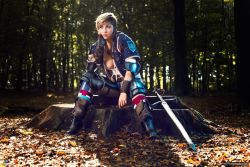Rule 34 | 1girl, breasts, brown hair, cosplay, fingerless gloves, forest, gloves, highres, jewelry, large breasts, nature, necklace, photo (medium), piercing, short hair, sitting, solo, sword, the witcher (series), tree, ves (the witcher), weapon