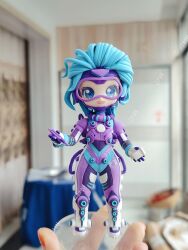 Rule 34 | 1girl, absurdres, ai chi jianguo xiaosong xu, animification, apex legends, artist&#039;s hand in frame, blue bodysuit, blue eyes, blue hair, blurry, blurry background, bodysuit, chinese commentary, clay (medium), gloves, goggles, highres, holding, holding pen, horizon (apex legends), looking at viewer, multicolored bodysuit, multicolored clothes, official alternate costume, open mouth, overfloater horizon, pen, photo (medium), purple bodysuit, short hair, smile, solo, unconventional media, white gloves