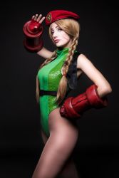 Rule 34 | 1girl, argentine (nationality), bare legs, bare shoulders, blonde hair, braid, cammy white, cammy white (cosplay), capcom, cosplay, curvy, gloves, green leotard, hand on own hip, hat, highleg, highleg leotard, highres, leotard, lips, long hair, looking at viewer, looking to the side, photo (medium), real life, shiny clothes, simple background, solo, sophie valentine, standing, street fighter, street fighter v, thong leotard, twin braids, very long hair, wide hips