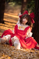 Rule 34 | 1girl, absurdres, autumn, autumn leaves, bare shoulders, bloomers, blunt bangs, blurry, bokeh, bow, bowtie, brown eyes, brown hair, closed mouth, cosplay photo, depth of field, detached sleeves, dutch angle, foot out of frame, gohei, hair bow, hakurei reimu, head tilt, highres, looking at viewer, no shoes, outdoors, photo (medium), red bow, red shirt, red skirt, shirt, skirt, skirt hold, sleeveless, sleeveless shirt, socks, solo, tamarie amareto, touhou, tree, underwear, white bloomers, white socks, yellow bow, yellow bowtie