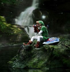Rule 34 | 1boy, artist request, blonde hair, blurry, blurry background, boots, brown footwear, brown gloves, cosplay, depth of field, fairy, fingerless gloves, forest, gauntlets, gloves, green hat, hat, instrument, lake, link, male focus, moss, music, nature, nintendo, ocarina, on floor, on rock, outdoors, photo (medium), plant, playing instrument, pointy ears, shield, sitting, solo, sword, the legend of zelda, tree, tunic, water, waterfall, weapon