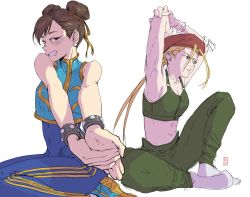 Rule 34 | 2girls, bare shoulders, beret, blonde hair, blue bodysuit, bodysuit, brown eyes, brown hair, cammy white, capcom, chun-li, double bun, edpan, green pants, arms up, hat, highres, long hair, looking at viewer, midriff, multiple girls, navel, pants, red headwear, sideways mouth, signature, simple background, sitting, smile, socks, street fighter, street fighter zero (series), stretching, studded bracelet, white background