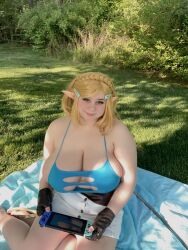Rule 34 | 1girl, bare shoulders, blanket, blonde hair, blue shirt, breasts, brown eyes, bush, cleavage, cosplay, eyelashes, female focus, grass, highres, huge breasts, legs, looking at viewer, minty lux, nintendo, nintendo switch, no bra, outdoors, photo (medium), plump, pointy ears, princess zelda, princess zelda (cosplay), sandals, shirt, shorts, sitting, skindentation, smile, solo, the legend of zelda, the legend of zelda: breath of the wild, tree, white shorts, wig