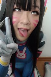 Rule 34 | 1girl, ahegao, asian, bodysuit, breasts, brown hair, cosplay, d.va (overwatch), facepaint, facial mark, overwatch, overwatch 1, photo (medium), solo, tongue, tongue out, v, whisker markings