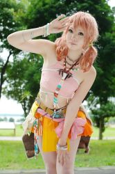Rule 34 | 1girl, belt, bracelet, cosplay, female focus, final fantasy, final fantasy xiii, grass, jewelry, looking at viewer, midriff, nature, necklace, oerba dia vanille, oerba dia vanille (cosplay), outdoors, photo (medium), pink shirt, plant, shirt, skirt, solo, standing, tree, twintails