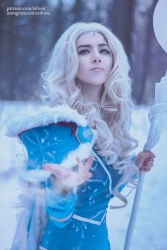 Rule 34 | 1girl, aqua eyes, armor, bare legs, blonde hair, blue cloak, blue dress, blue eyes, chain, cloak, cosplay, crystal, crystal maiden, crystal maiden (cosplay), dota (series), dota 2, dress, eyelashes, eyeliner, eyeshadow, forest, fur trim, gloves, highres, knees, lips, long hair, looking at viewer, makeup, nature, nose, outstretched hand, photo (medium), self-upload, signature, snow, snowing, solo, staff, standing, winter