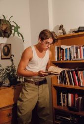 Rule 34 | 1boy, atlantis: the lost empire, belt, book, bookshelf, cosplay, desk, disney, glasses, indoors, male focus, milo thatch, milo thatch (cosplay), open book, pants, photo (medium), picture frame, plant, potted plant, reading, shelf, solo, tank top, theodore roosevelt