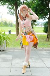 Rule 34 | 1girl, belt, boots, bracelet, cosplay, female focus, final fantasy, final fantasy xiii, grass, jewelry, midriff, navel, necklace, oerba dia vanille, oerba dia vanille (cosplay), outdoors, pink shirt, shirt, skirt, solo, standing, tiles, tree, twintails