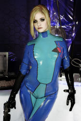 Rule 34 | airbrushed, arms at sides, blonde hair, bodysuit, cameltoe, cosplay, cosplay photo, cowboy shot, eyelashes, gun, indoors, latex, latex suit, leaning to the side, lowres, metroid, metroid: zero mission, nintendo, photo (medium), samus aran, skin tight, solo, standing, weapon, zero suit