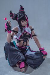 Rule 34 | 1girl, arm strap, black gloves, black hair, black pants, blue nails, candy, cosplay photo, crop top, fingerless gloves, food, gloves, hair horns, hair over one eye, han juri, highres, holding, holding candy, holding food, holding lollipop, lollipop, looking at viewer, mamichi (mamichi 913), multicolored hair, nail polish, navel, one eye covered, pants, photo (medium), pink eyes, pink hair, shadow, sitting, smile, solo, spikes, streaked hair, street fighter, v-shaped eyebrows