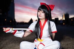 1girl ainu_clothes black_hair breasts cosplay fingerless_gloves gloves hair_ribbon half-closed_eyes highres legs long_hair nakoruru pants parted_lips pink_lips ribbon samurai_spirits sitting small_breasts snk solo the_king_of_fighters thighs weapon