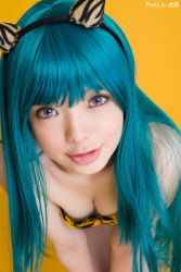 Rule 34 | 1girl, animal print, aqua hair, asian, bikini, blue hair, blurry, breasts, cleavage, color contacts, cosplay, depth of field, fake horns, highres, horns, indoors, leaning forward, light smile, long hair, looking at viewer, lum, lum (cosplay), namada, photo (medium), purple eyes, simple background, small breasts, solo, strapless, strapless bikini, swimsuit, tiger print, urusei yatsura, yellow background