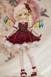 Rule 34 | 1girl, adapted costume, belt, blonde hair, blurry, blurry background, brown belt, character doll, crystal, depth of field, doll, fangs, flandre scarlet, frilled skirt, frills, full body, hat, head tilt, highres, medium hair, miyako sasara, mob cap, multicolored wings, one side up, open mouth, petticoat, photo (medium), puffy short sleeves, puffy sleeves, red eyes, red skirt, red vest, shirt, short sleeves, skirt, solo, standing, touhou, vest, white hat, white shirt, wings, wrist cuffs