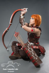 Rule 34 | 1girl, arrow (projectile), boots, bow (weapon), cosplay, dragon age, highres, indian style, leliana (dragon age), nail polish, orange hair, photo (medium), pteruges, quiver, sitting, sleeveless, solo, vambraces, weapon