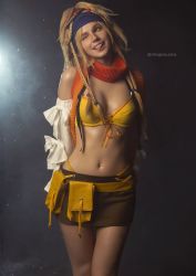 Rule 34 | 1girl, arms behind back, bare shoulders, belt, belt pouch, bikini, blonde hair, braid, breasts, brown skirt, cleavage, cosplay, cosplay photo, cowboy shot, detached sleeves, final fantasy, final fantasy x, gradient background, green eyes, headband, highres, long hair, long sleeves, looking away, looking to the side, medium breasts, miniskirt, multiple braids, navel, one eye closed, open mouth, photo (medium), pouch, red scarf, rikku (ff10), rikku (ff10) (cosplay), scarf, skirt, solo, stomach, swimsuit, teeth, tongue, tongue out, twitter username, upper teeth only, yellow bikini