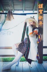 Rule 34 | 1girl, absurdres, bare tree, blonde hair, brown headwear, closed mouth, cosplay photo, detached sleeves, from side, full body, hair ribbon, hat, highres, leaning back, looking at viewer, moriya suwako, no shoes, noa813, outdoors, photo (medium), pyonta, red ribbon, ribbon, ribbon-trimmed sleeves, ribbon trim, sleeves past fingers, sleeves past wrists, tassel, thighhighs, touhou, tree, white thighhighs, wide sleeves, wooden deck, yellow tassel