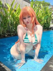 Rule 34 | 1girl, arm tattoo, artist request, bikini, breasts, breasts squeezed together, cosplay, fingernails, green bikini, highres, kneeling, large breasts, lips, long hair, navel, one piece, orange hair, palm tree, photo (medium), plant, pool, real life, sharp fingernails, smile, solo, swimsuit, tattoo, tattoo on neck, tree