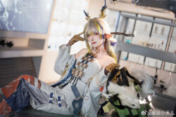 Rule 34 | 1girl, arknights, bare shoulders, blonde hair, blue hair, branch, brown gloves, chaojixiaoheer, closed mouth, collarbone, commentary request, cosplay, dragon horns, earrings, eyeshadow, gloves, green eyes, grey hair, grey pants, highres, holding, horns, indoors, jacket, jewelry, laboratory, long hair, long sleeves, looking at viewer, makeup, multicolored hair, necklace, open clothes, open jacket, pants, photo (medium), pointy ears, red eyeshadow, shirt, shu (arknights), shu (arknights) (cosplay), sitting, skirt, smile, solo, streaked hair, stuffed animal, stuffed dragon, stuffed toy, weibo watermark, white jacket, white shirt, white skirt