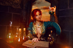 Rule 34 | 1girl, beaker, blurry, book, braid, breasts, center opening, circlet, cleavage, cloud, cosplay, costume, depth of field, dress, eyeliner, eyeshadow, flask, freckles, helly von valentine (disharmonica), indoors, jewelry, long hair, looking at object, makeup, medium breasts, necklace, no bra, parted lips, pendant, photo (medium), pinky out, red hair, robe, side braids, sitting, sky, solo, table, the witcher (series), triss merigold, triss merigold (cosplay), upper body, window
