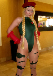 Rule 34 | 1girl, beret, blonde hair, bodypaint, boots, braid, breasts, cammy white, cammy white (cosplay), capcom, cosplay, earrings, fingerless gloves, garrison cap, gauntlets, gloves, hands on own hips, hat, high collar, highleg, highleg leotard, highres, ikuy, jewelry, leotard, nose piercing, pantyhose, photo (medium), piercing, solo, street fighter, swept bangs, thighs, thong leotard, twin braids