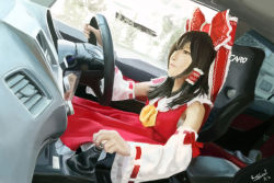 Rule 34 | black hair, blouse, bow, brown eyes, brown hair, car interior, car seat, cosplay, dated, detached sleeves, driving, frilled bow, frills, gear shift, hair bow, hair tubes, hakurei reimu, hakurei reimu (cosplay), highres, long hair, noelsahelangi, nontraditional miko, photorealistic, realistic, red bow, red shirt, red skirt, shirt, skirt, solo, touhou, vehicle interior, wheel, wide sleeves, yellow neckwear