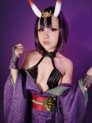 Rule 34 | 1girl, bare shoulders, breasts, cleavage, cosplay, fate/grand order, fate (series), female focus, highres, horns, looking at viewer, mexican (nationality), photo (medium), purple background, purple eyes, purple hair, rabbit.exe, real life, short hair, shuten douji (fate), shuten douji (fate) (cosplay), simple background, skin-covered horns, small breasts, solo