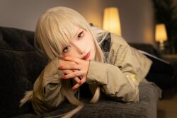 Rule 34 | 1girl, black pants, blonde hair, blue eyes, blurry, blurry background, brown jacket, cosplay, cosplay photo, couch, gigi andalusia, gundam, gundam hathaway&#039;s flash, highres, hisage, jacket, lamp, long hair, looking at viewer, lying, nail polish, on couch, pants, photo (medium), red nails, solo