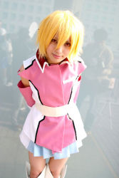 Rule 34 | 1girl, arms behind back, bare shoulders, blonde hair, blue skirt, boots, closed mouth, cosplay, cosplay photo, cowboy shot, elbow gloves, gloves, gundam, gundam seed, gundam seed destiny, hair between eyes, looking back, miniskirt, outdoors, photo (medium), pink gloves, pleated skirt, red eyes, sash, short hair, skirt, sleeveless, smile, solo focus, standing, stellar loussier, thigh boots, thighhighs, white footwear