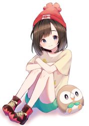 Rule 34 | 1girl, bare legs, beanie, blush, brown hair, closed mouth, commentary request, creatures (company), crossed arms, eyelashes, floral print, game freak, gen 7 pokemon, green shorts, grey eyes, hat, highres, kajiki ngtk9, knees, medium hair, nintendo, pokemon, pokemon (creature), pokemon sm, red headwear, rowlet, selene (pokemon), shirt, shoes, short shorts, short sleeves, shorts, simple background, sitting, smile, sneakers, t-shirt, white background